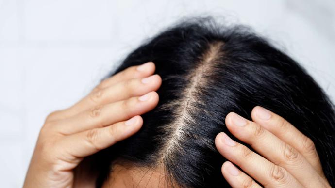 Mains de femme de chaque côté de ses cheveux noirs avec raie au milieu