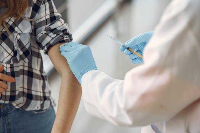 Jeune femme chemise à carreaux qui se fait vacciner par un médecin à blouse blanche et gants bleus qui tient une aiguille