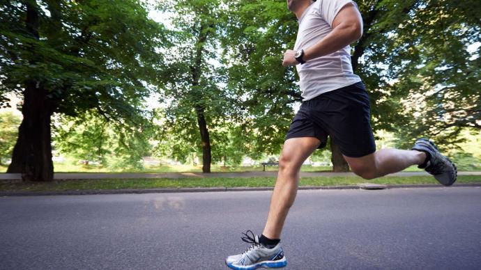 Homme avec tee-shirt blanc et short noir qui court sur une route avec des arbres derrière