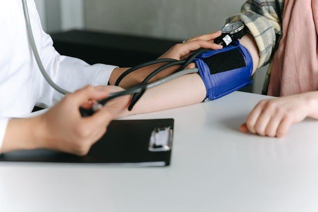 Médecin en blouse blanche qui prend la tension d'une patiente avec chemise à carreaux