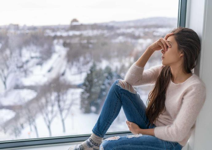 Jeune femme la main sur les yeux assise devant une fenêtre en hiver