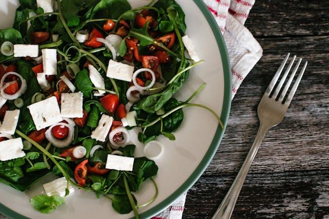 Assiette de salade, tomates cerises et feta posée sur un torchon avec une fourchette à côté