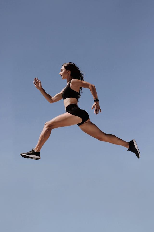 Jeune femme brassière, short et baskets noires courant dans le ciel bleu
