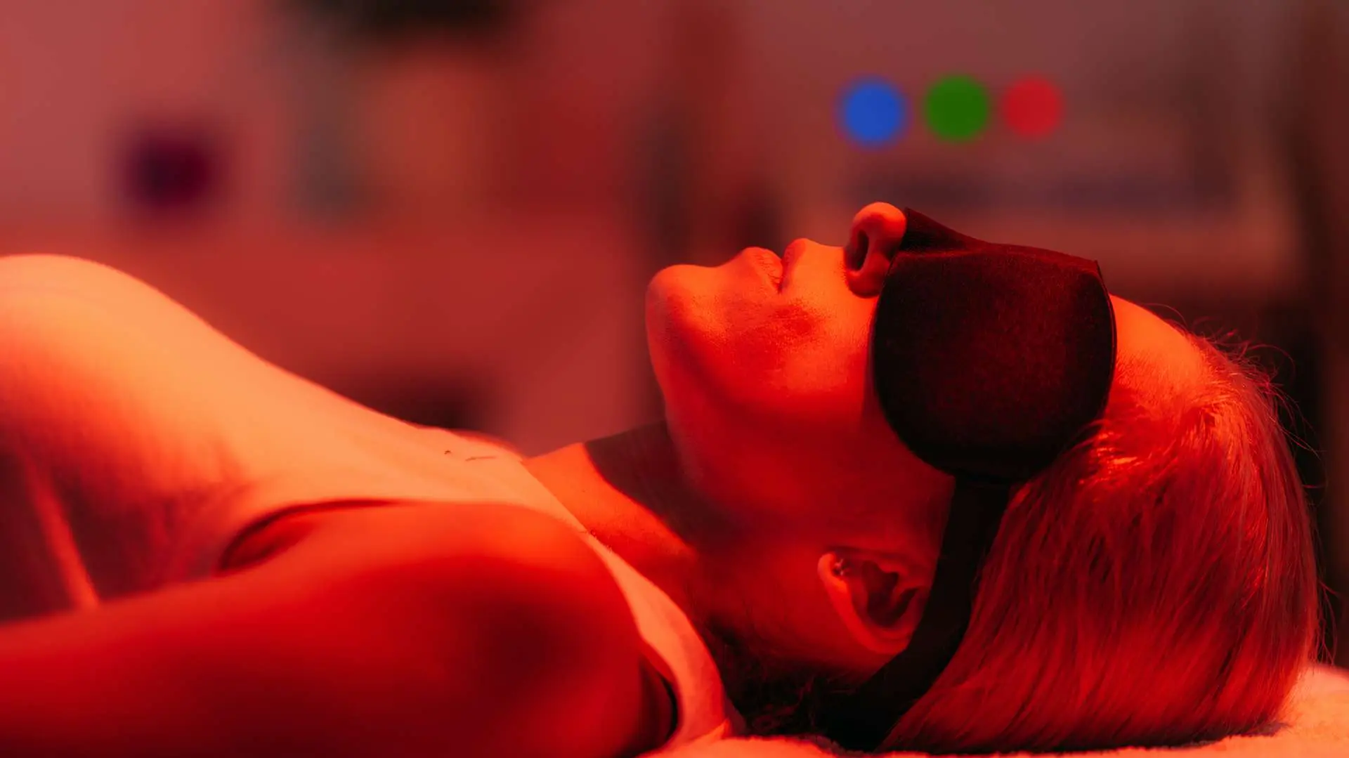 Femme allongée avec bandeau noir sur les yeux pendant une séance de thérapie à la lumière rouge