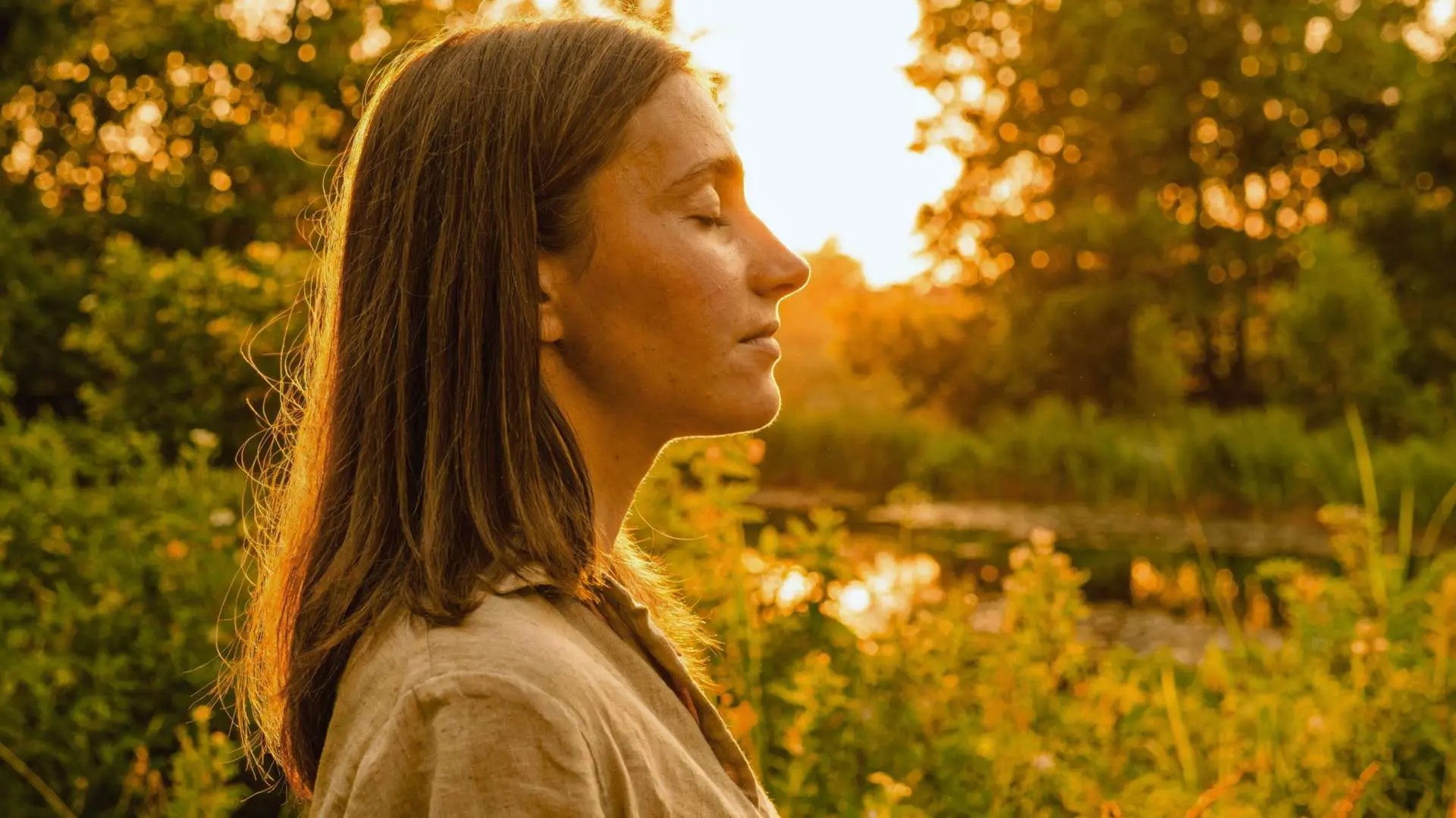 Jeune femme aux cheveux  longs de profil les yeux femras dans la nature avec lumière d'un soleil automnal 