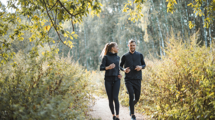 Femme et homme habillés en noir qui courent dans une forêt