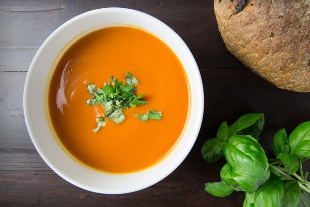 Potage orange avec feuilles de basilic au-dessus et à côté avec une miche d emain sur une table marron