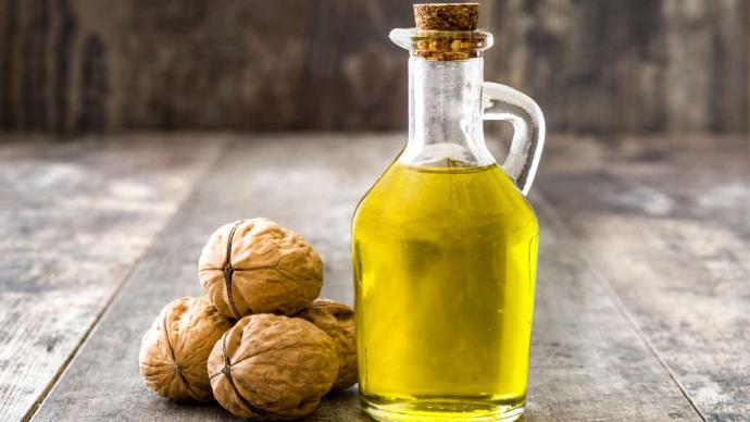 Bouteille d'huile de noix avec quatre noix à côté sur une table en bois gris