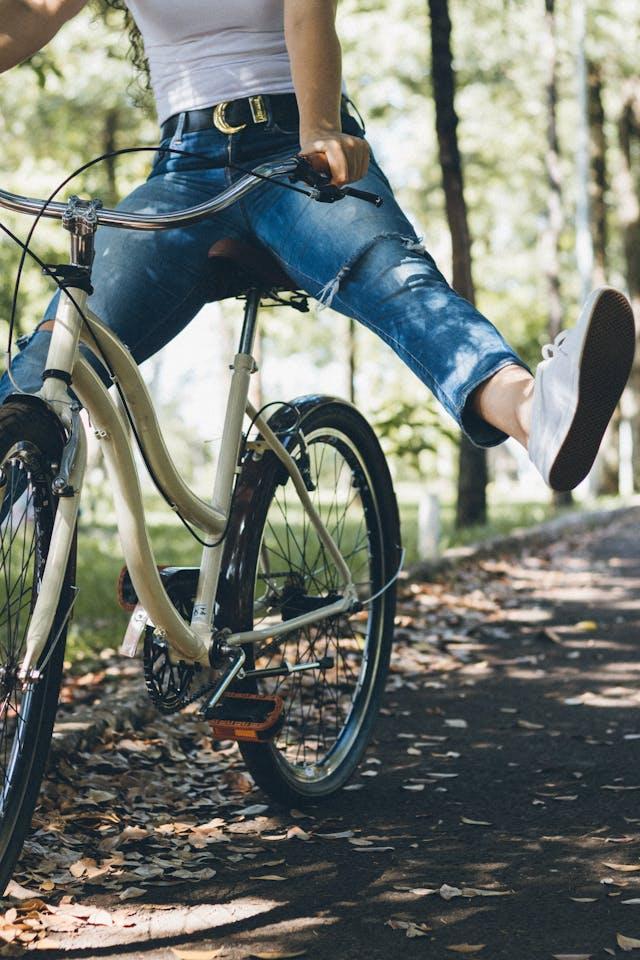 Femme haut et baskets blanches, jean bleu sur un vélo blanc les jambes écartées sur chemin de forêt