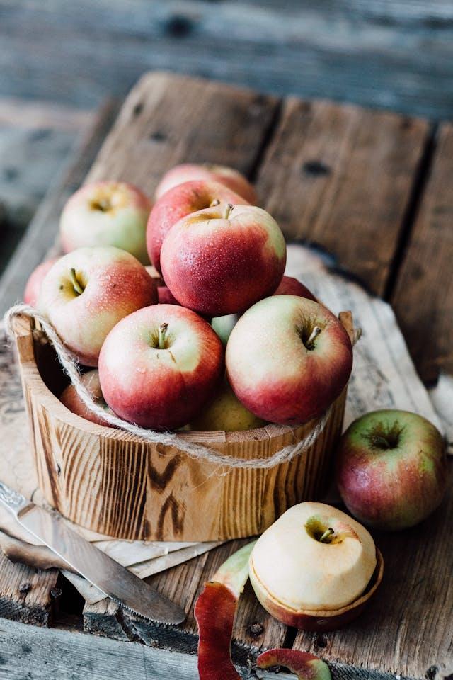 Pommes entières et une pelée dabs seau en boic sur table en bois avec un couteau