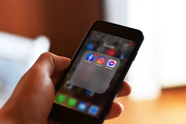 Main qui tient un téléphone avec icônes réseaux sociaux sur l'écran