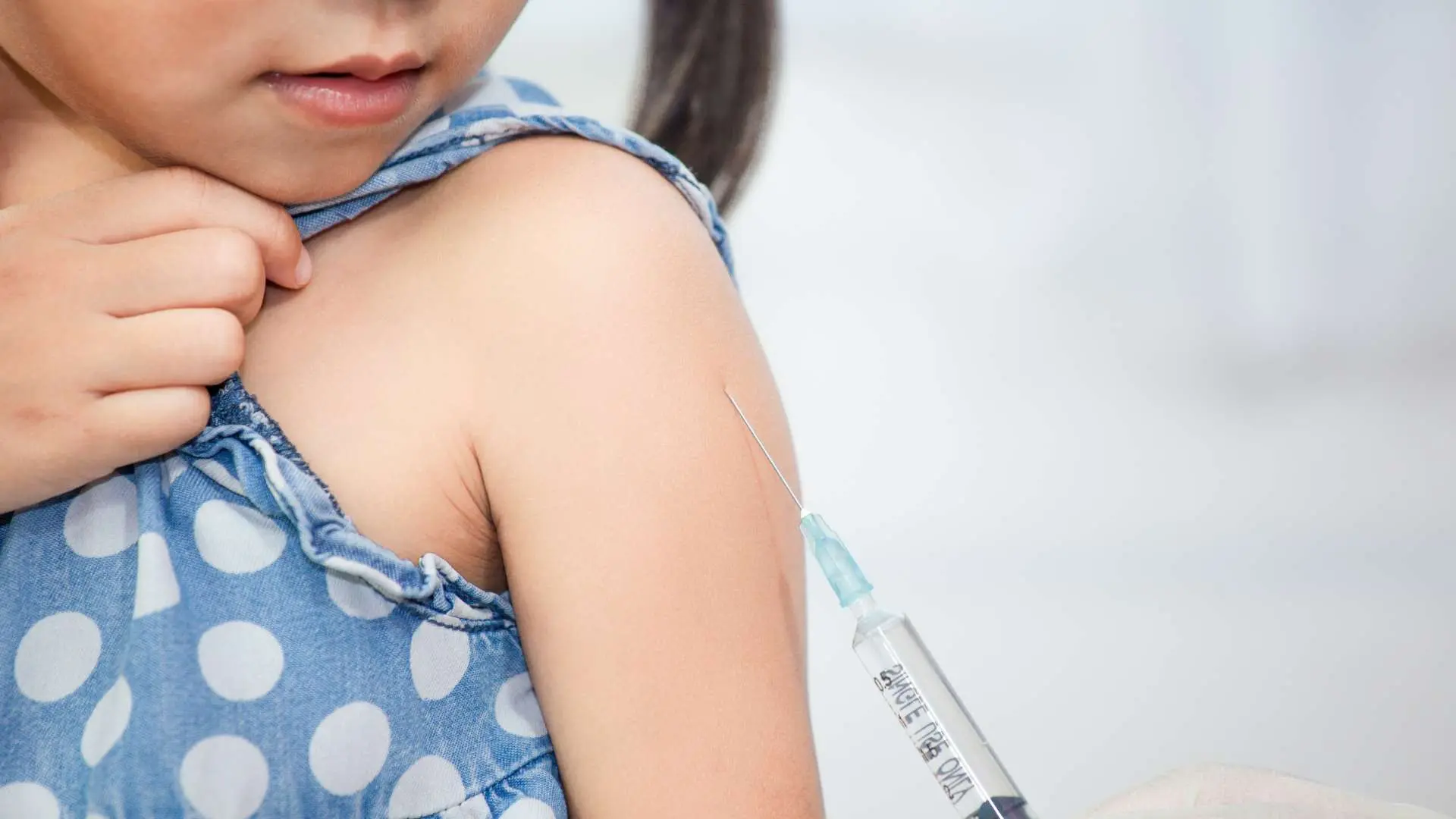 Petite fille avec robe débardeur en jean bleu à pois blanc qui se fait vacciner dans le bras