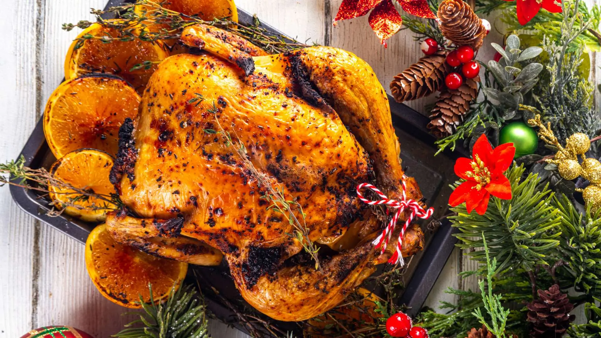 Vue de haut dinde de Noël dans un plat noir avec tranches d'oranges et branches de sapin, pommes de pins, fleur rouge à côté