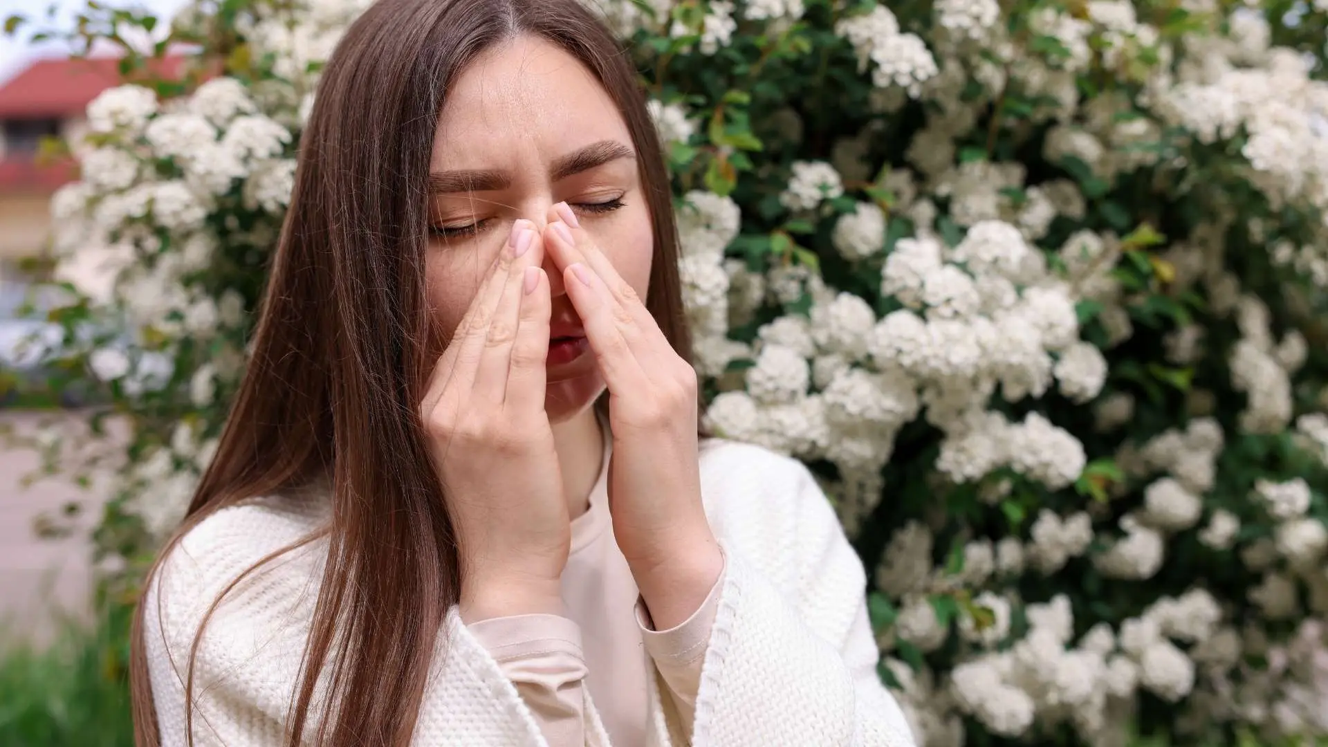 Jeune femme allergique devant massif avec fleurs blanches
