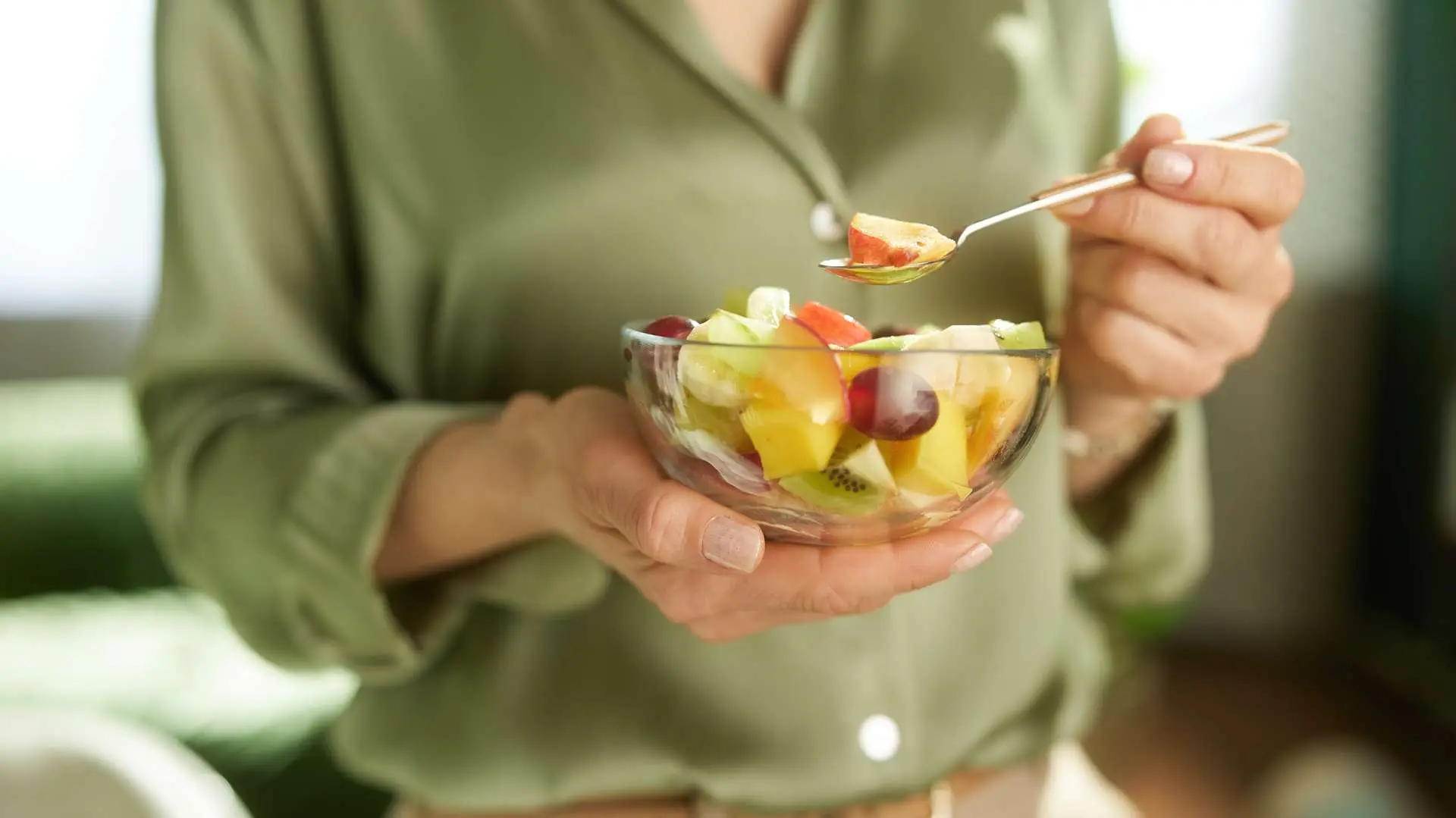 Buste de femme en chemisier satiné vert qui tient une coupelle transparente de salade de fruits