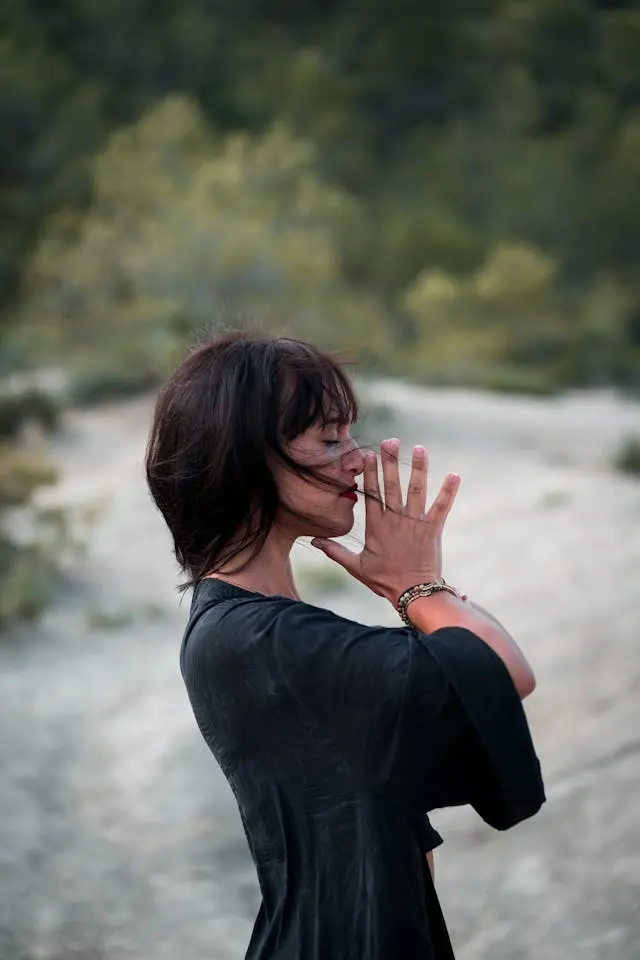Femme de profil qvec rivière et arbres en arrière-plan les yeux fermés et les mains jointes devant son visage