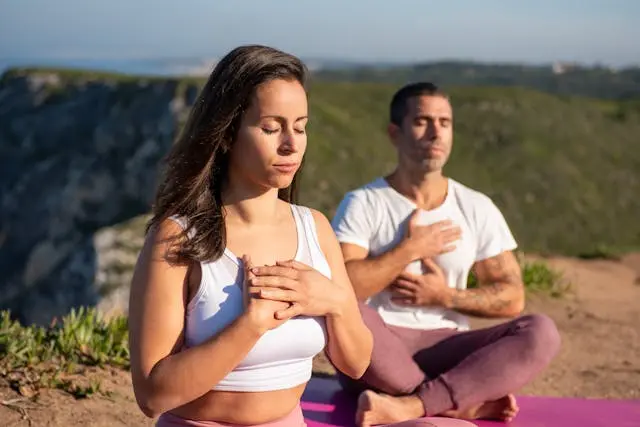 Couple assis en tailleur les yeux fermés sur une falaise pratiquant la cohérence cardiaque