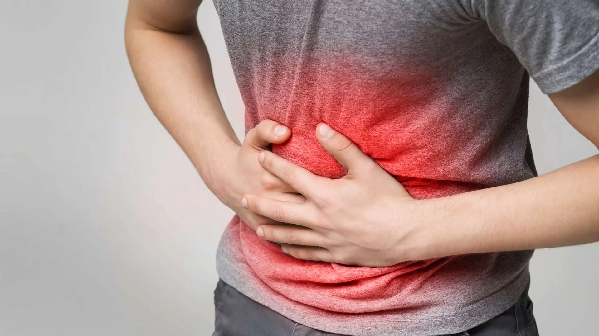 Gros plan ventre d'homme en tee-shirt gris qui souffre du pancréas avec douleur rouge et mains sur le ventre