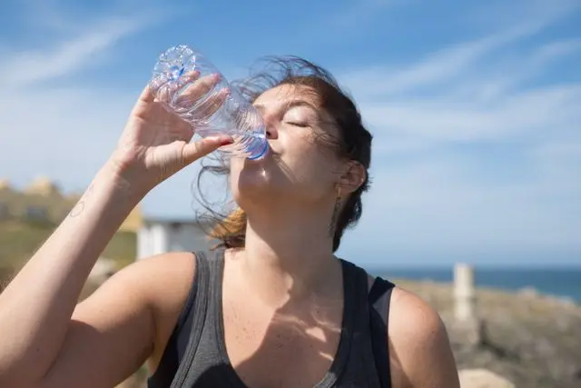 Jeune femme qui boit de l'eau dans une petite bouteille abec paysage et mer en arrière-plan