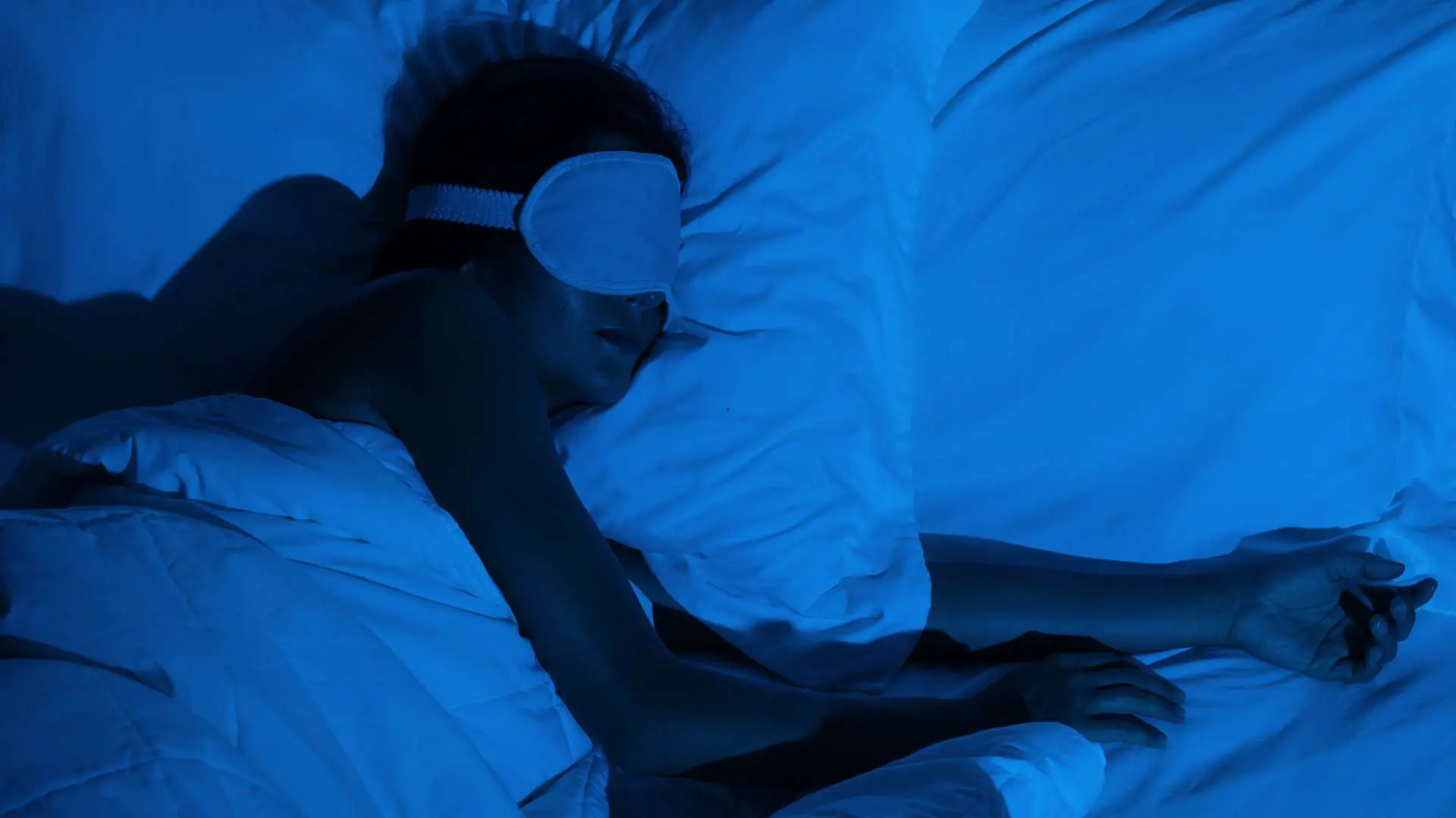 Femme qui dort sur le côté dans des draps blancs avec un masque blanc sur les yeux